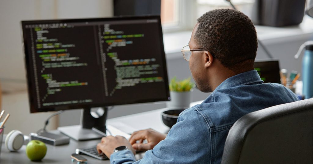 Person writing code on a computer in a modern workspace.