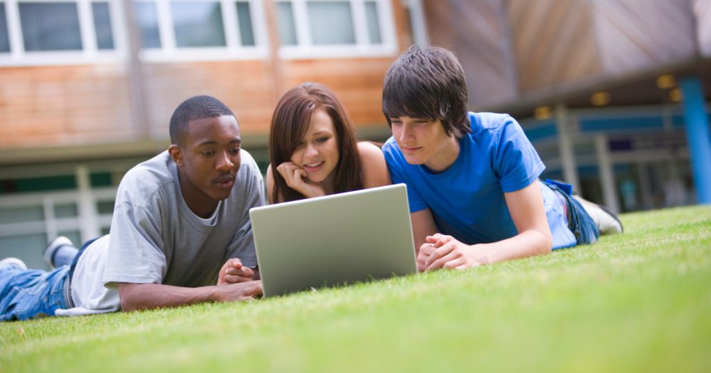 Diverse group of students studying on a laptop outdoors, collaborating on a tech project.